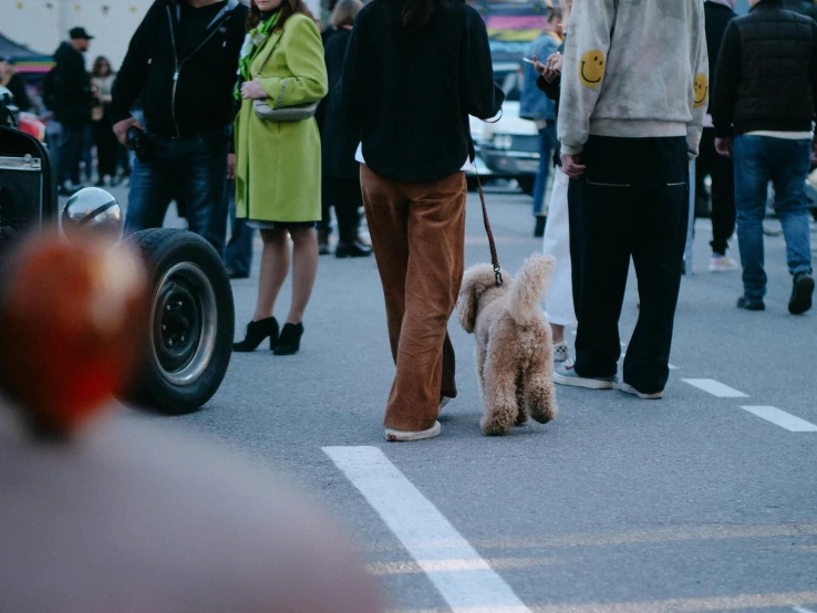 a man in brown pants and white jacket walking his dog through a busy city