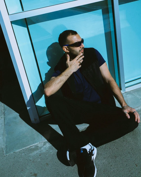 a man sitting on the sidewalk by some glass walls