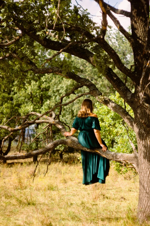 a woman in a green dress walking in front of a tree