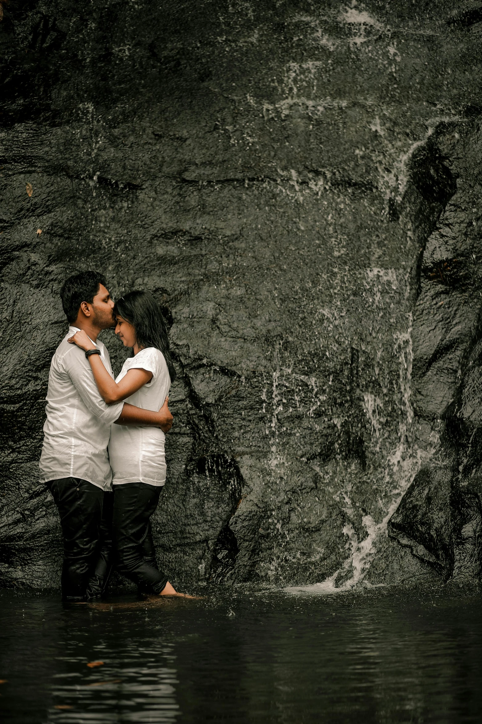 the couple emce as they stand in the water by the rocks