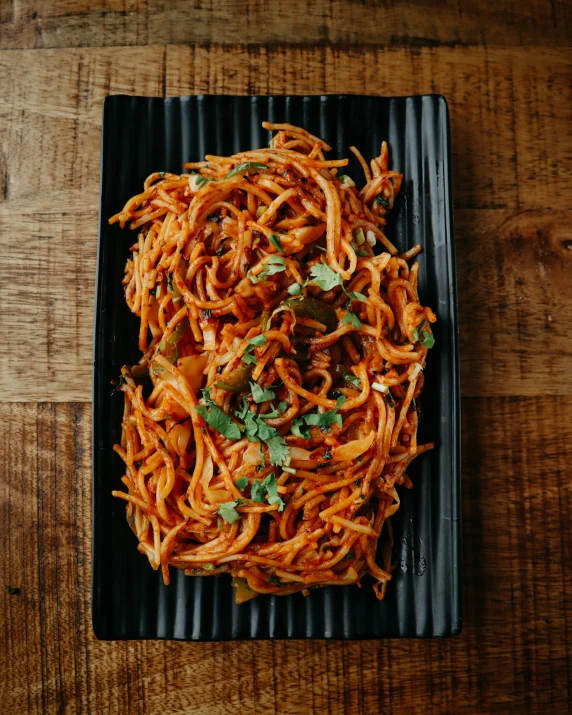 a black plate filled with spaghetti on top of a wooden table