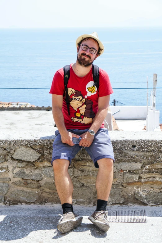 man with glasses sitting in front of water and rocks