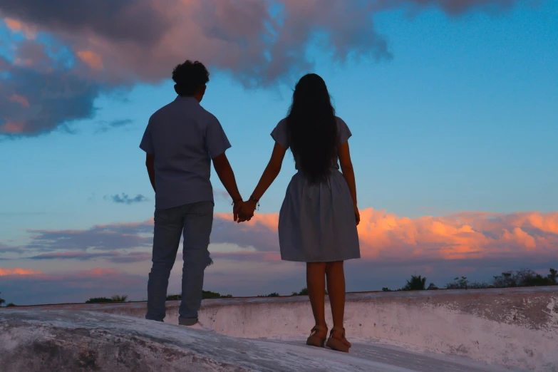 a man and woman holding hands on top of a hill