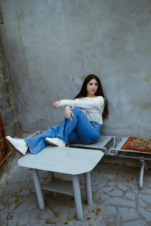 a beautiful young woman sitting on top of a white bench