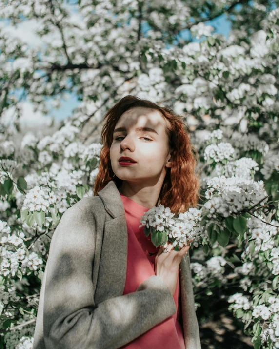 a woman holding flowers with eyes closed in front of trees