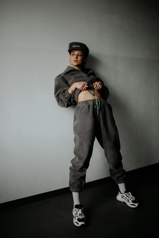 a  is standing by a wall in a gray sweatshirt and sweatpants