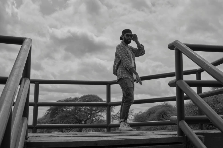 black and white pograph of man standing on wooden railing near water