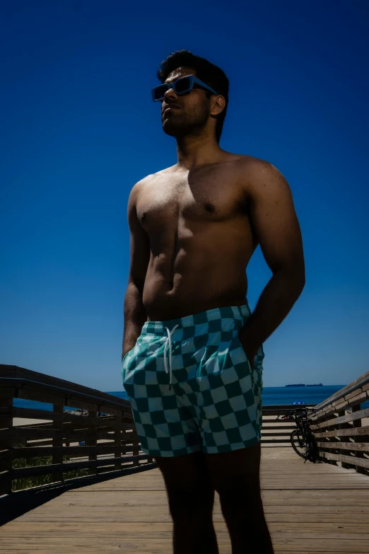 a young man wearing swimming trunks stands on a boardwalk