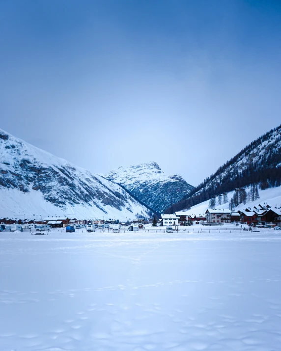 the snowy mountains behind houses are dotted by a line of trees