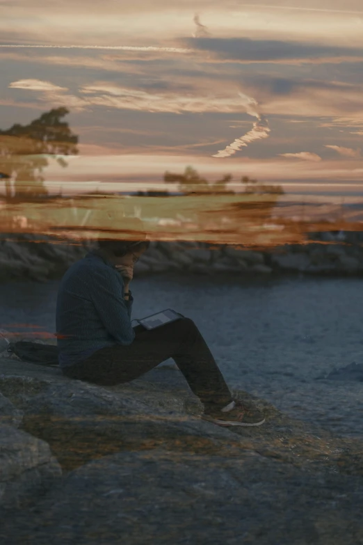 a person sitting on rocks looking at a laptop