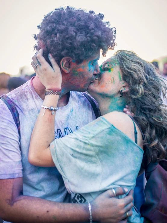 a man and woman kissing in front of people with holi makeup on