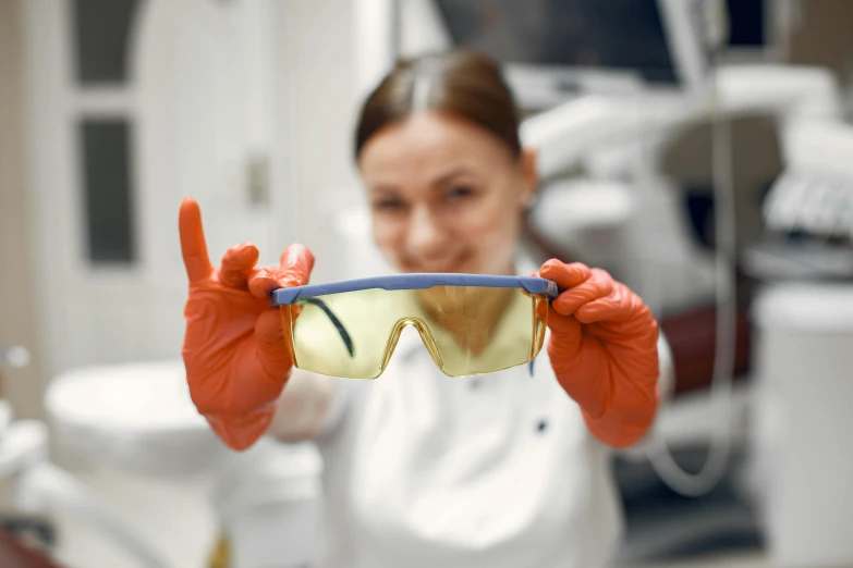 a woman wearing orange gloves holding up sunglasses