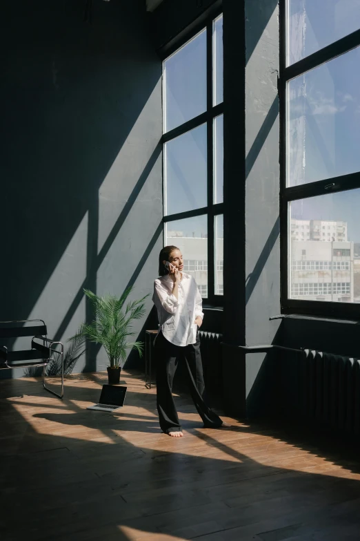 a woman standing next to a window talking on a cell phone