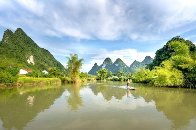 a man riding a paddle board in a river surrounded by mountains