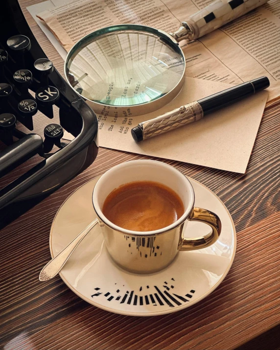 a cup of coffee sits on a saucer next to a paper and old typewriter