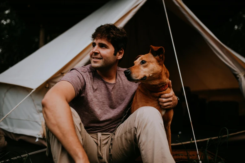 a man sitting next to a dog near a tent