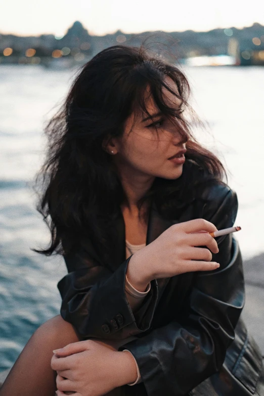 a woman is sitting by the river smoking a cigarette