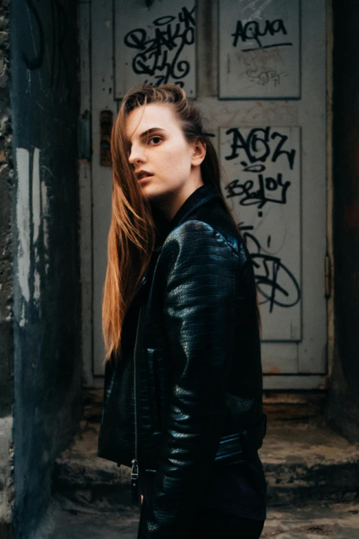 a young woman with long red hair standing in front of graffiti covered doors