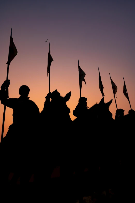 military men holding flags are silhouetted against a dusk sky