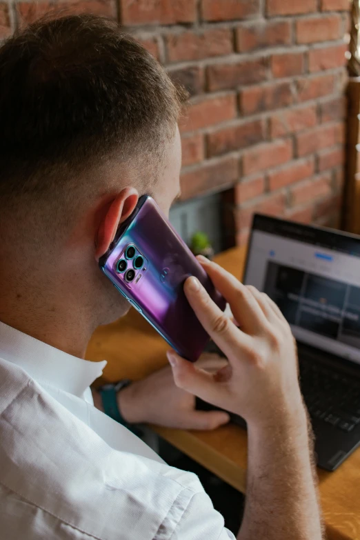 the man is talking on his phone in front of his laptop