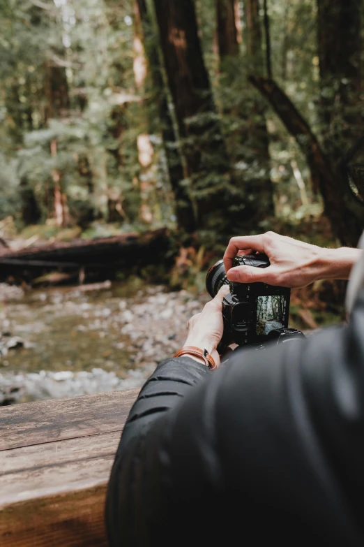 person using camera to take pictures by a stream