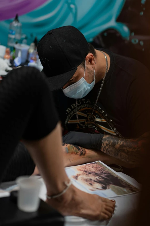 a man is working on a tattoo while wearing a face mask