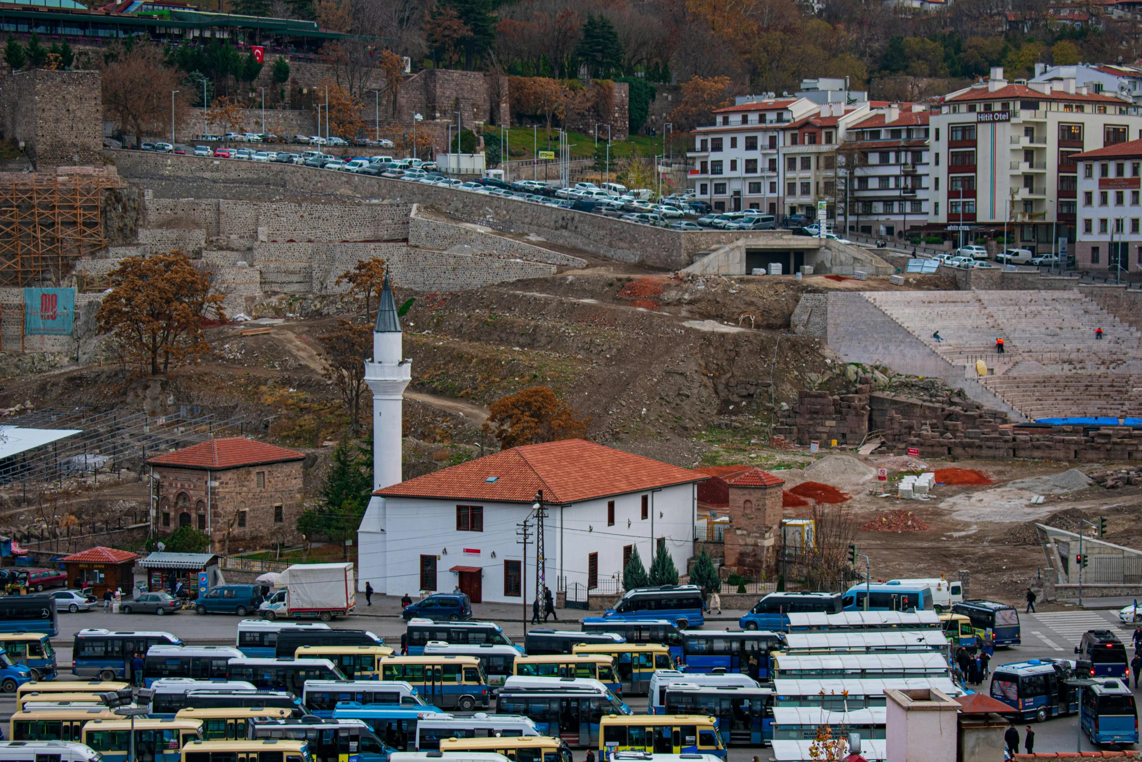 lots of buses in the parking lot near buildings