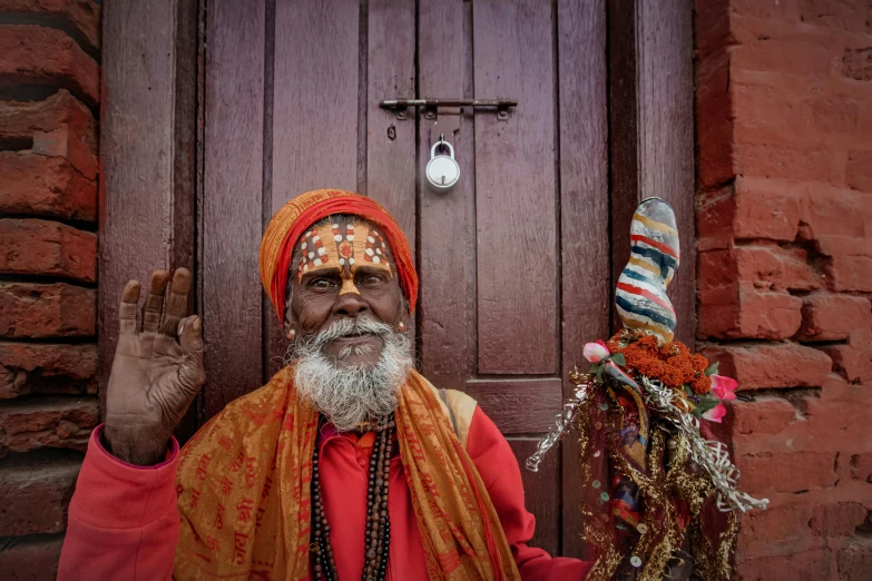 an indian man wearing red poses with his hand raised in front of a door