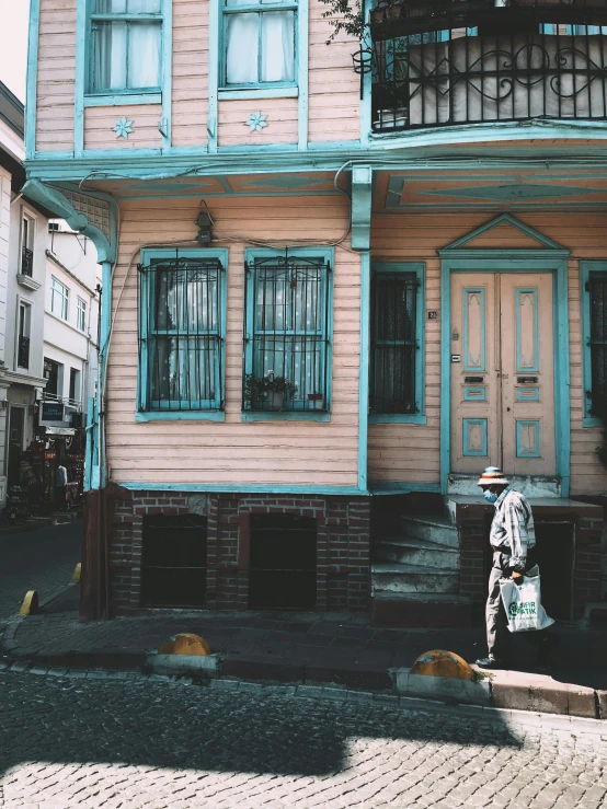 a person in a hat walking by an old pink house