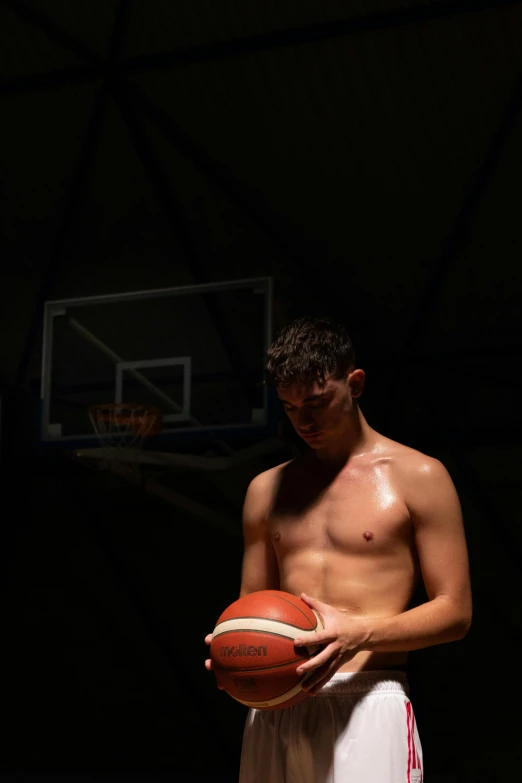 a shirtless man holding a basketball standing in front of a basket