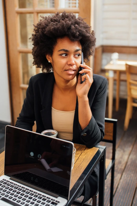 a woman sitting at a table with a laptop and cellphone in her hand