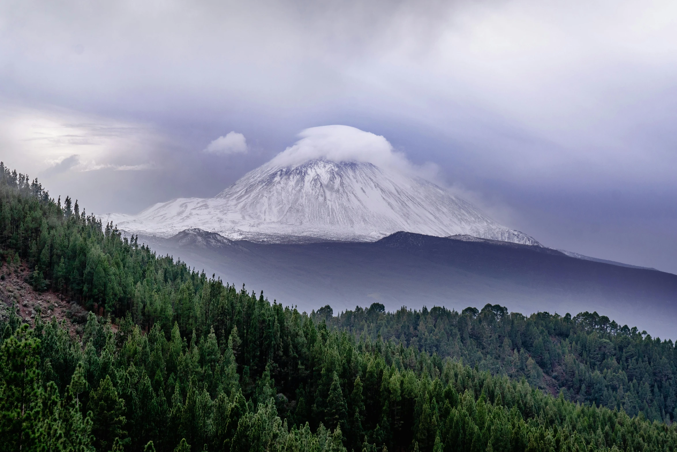 a view of a snow covered mountain under clouds