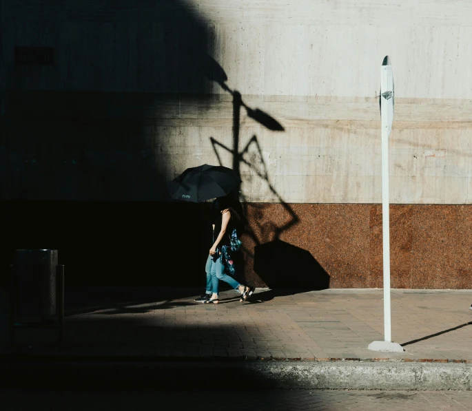 man carrying a black umbrella in the shadows with his shadow from the pole