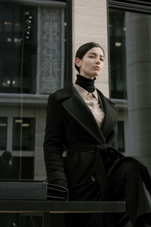 woman in black coat sitting at bench outside building