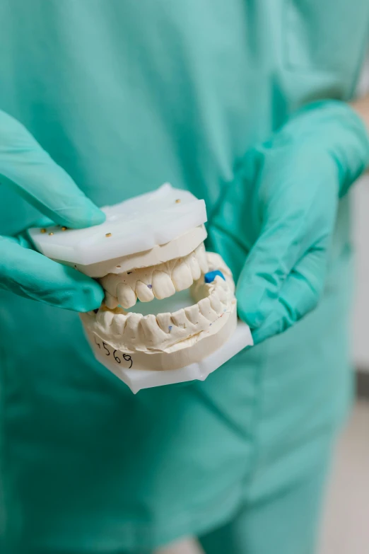 a dental technician with gloves on holding a model