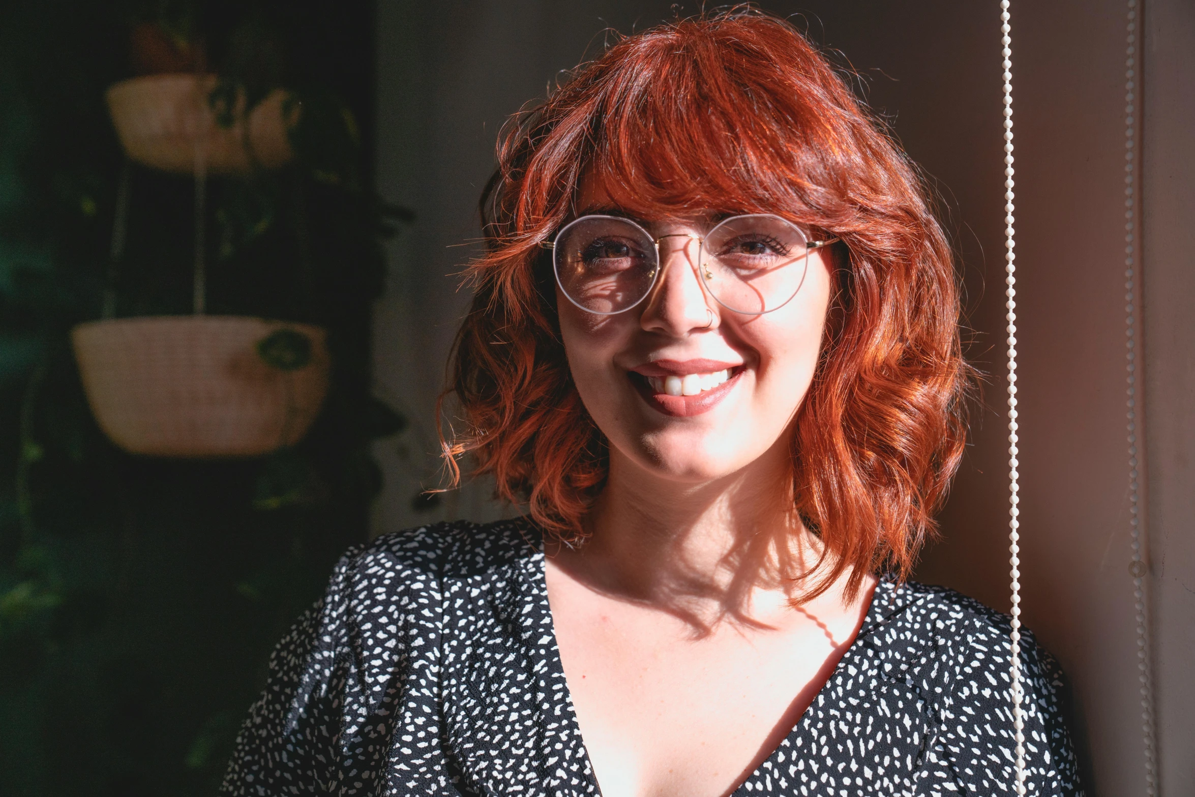 a woman with red hair wearing glasses and a black floral top