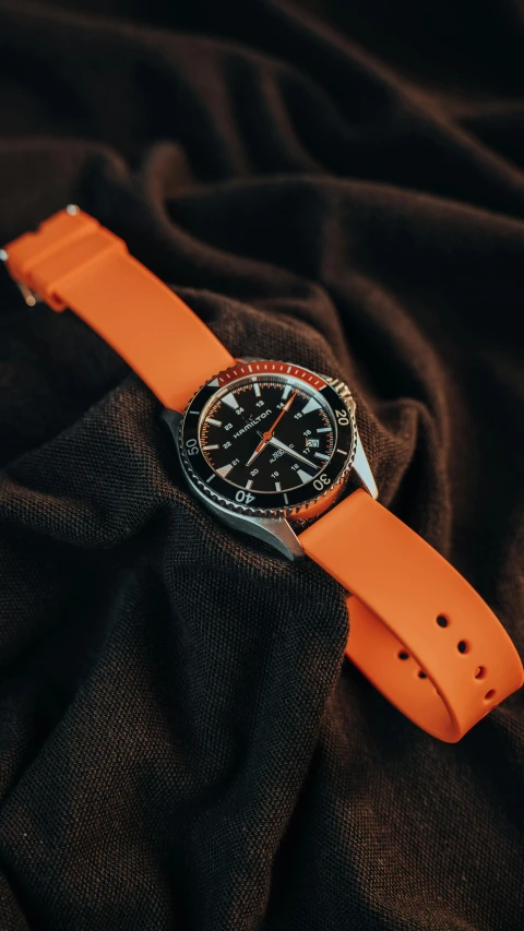 an orange strap is worn on the wrist of a black and white watch