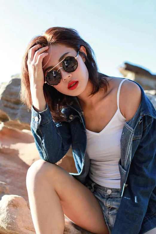 a young woman is sitting on rocks wearing sunglasses