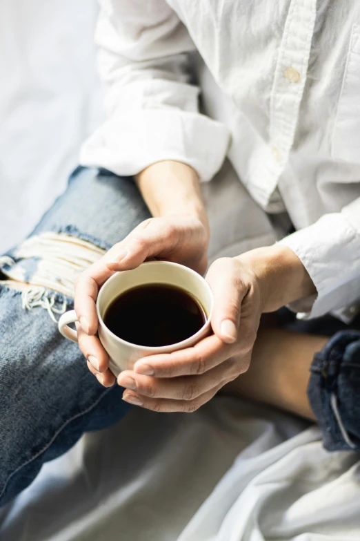 a person holding a cup of coffee while sitting in the bed