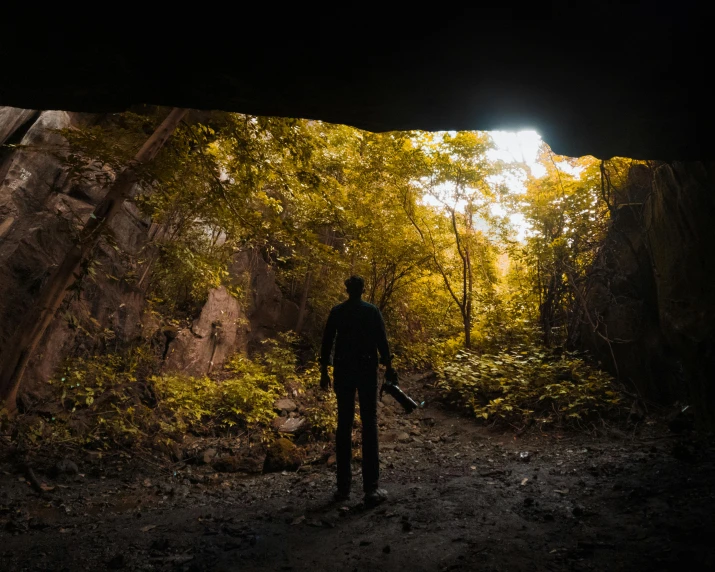 the man in the dark is standing next to a rock arch