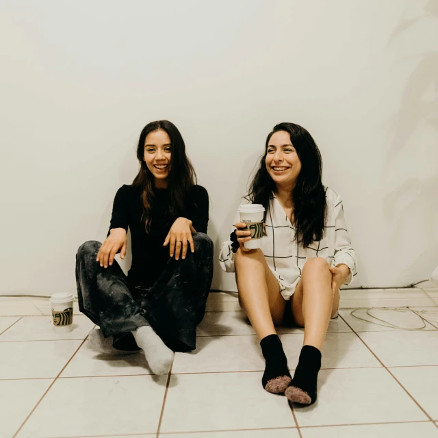 two women sitting side by side with a drink in hand