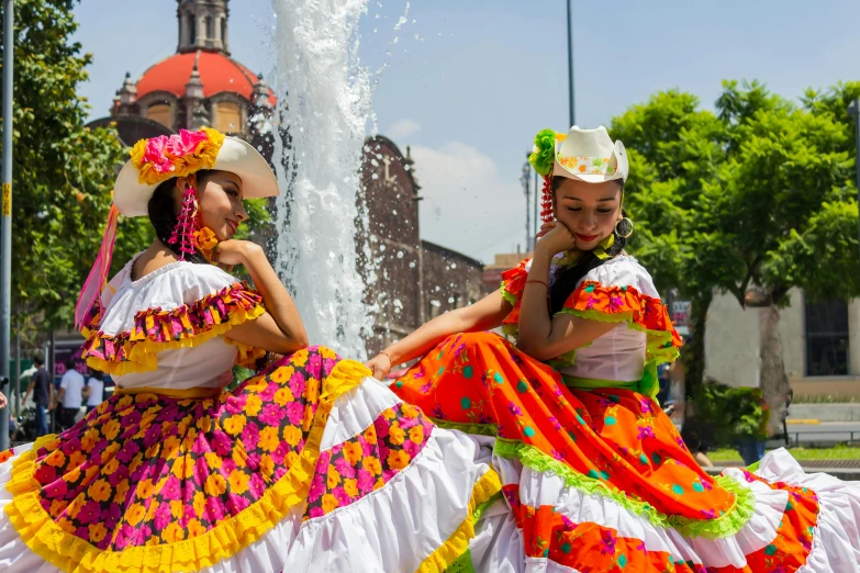 two people dressed in colorful clothing posing in front of a fountain