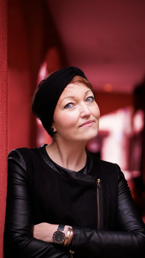 a woman in black leather jacket and red wall