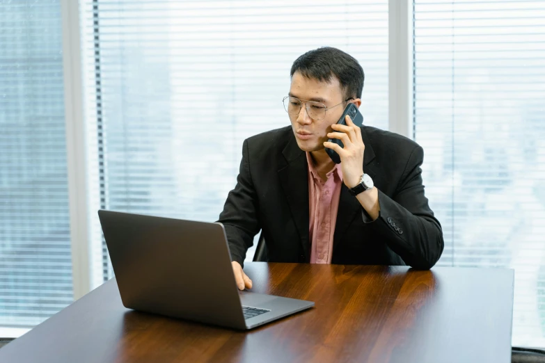 an asian man on a cell phone and laptop at a table