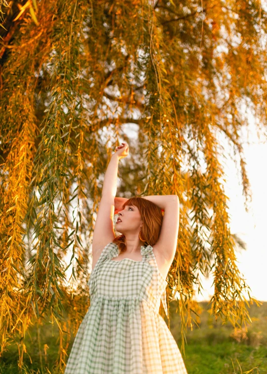 a girl in a dress holds up leaves and looks up