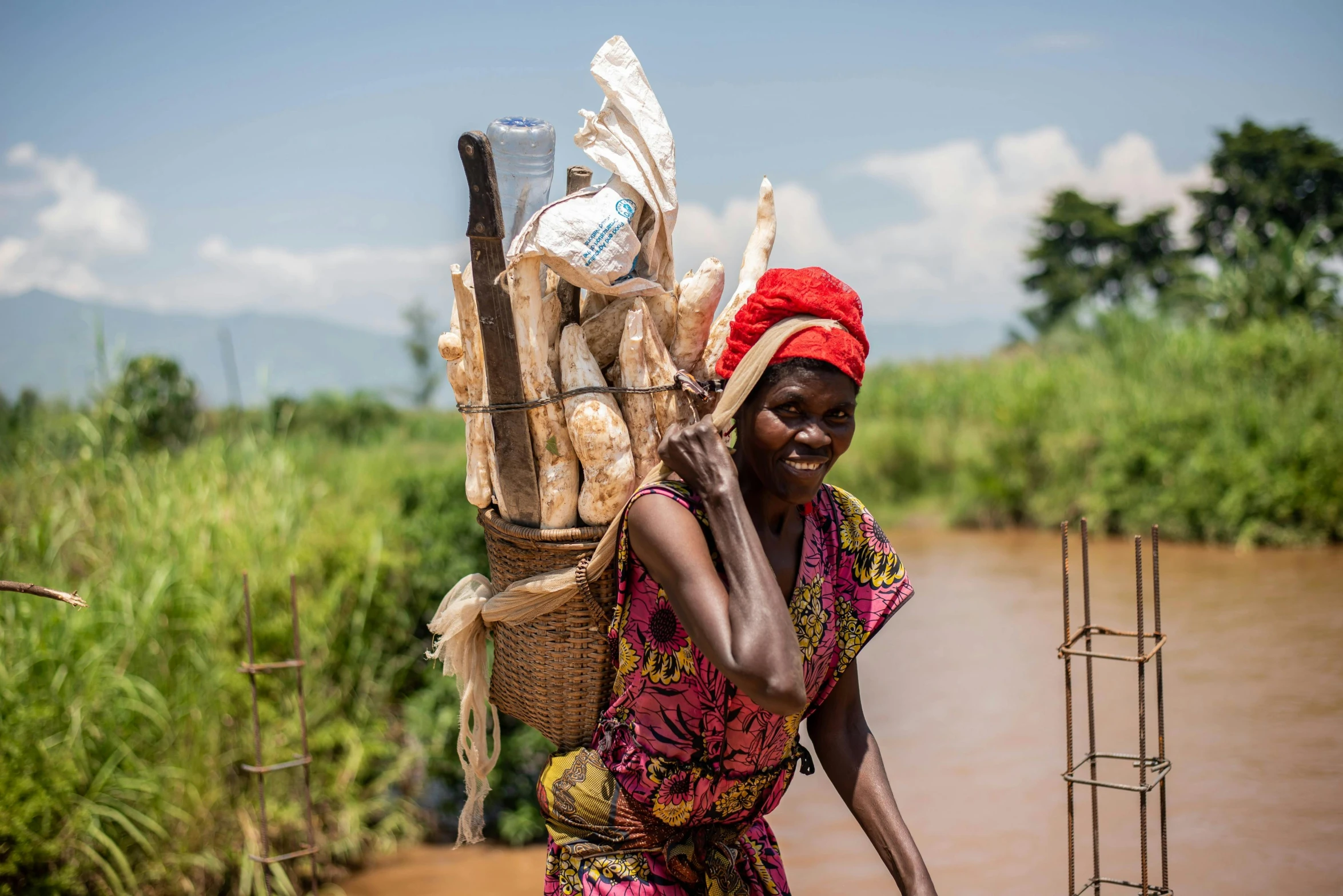 a woman carrying wood sticks down the river bank