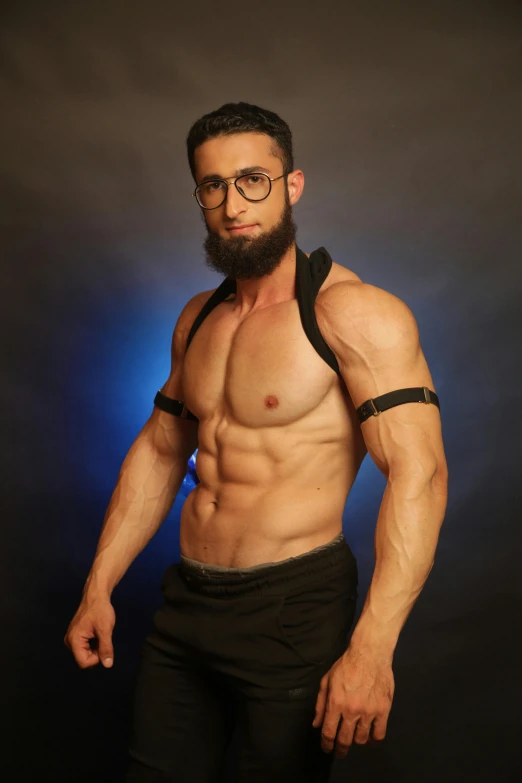 shirtless man wearing glasses and black suspenders standing in front of a dark background