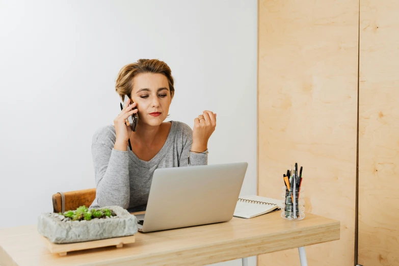 a woman holding her cell phone up to her ear as she talks on her laptop