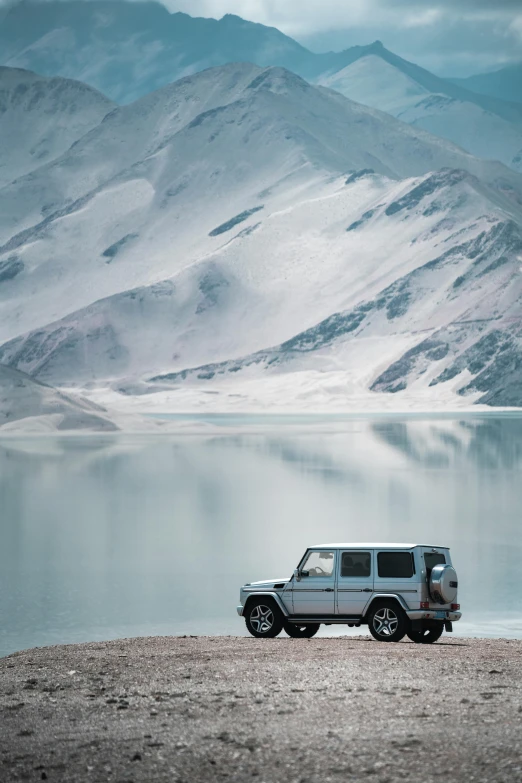 a suv parked on the shore with mountains in the background