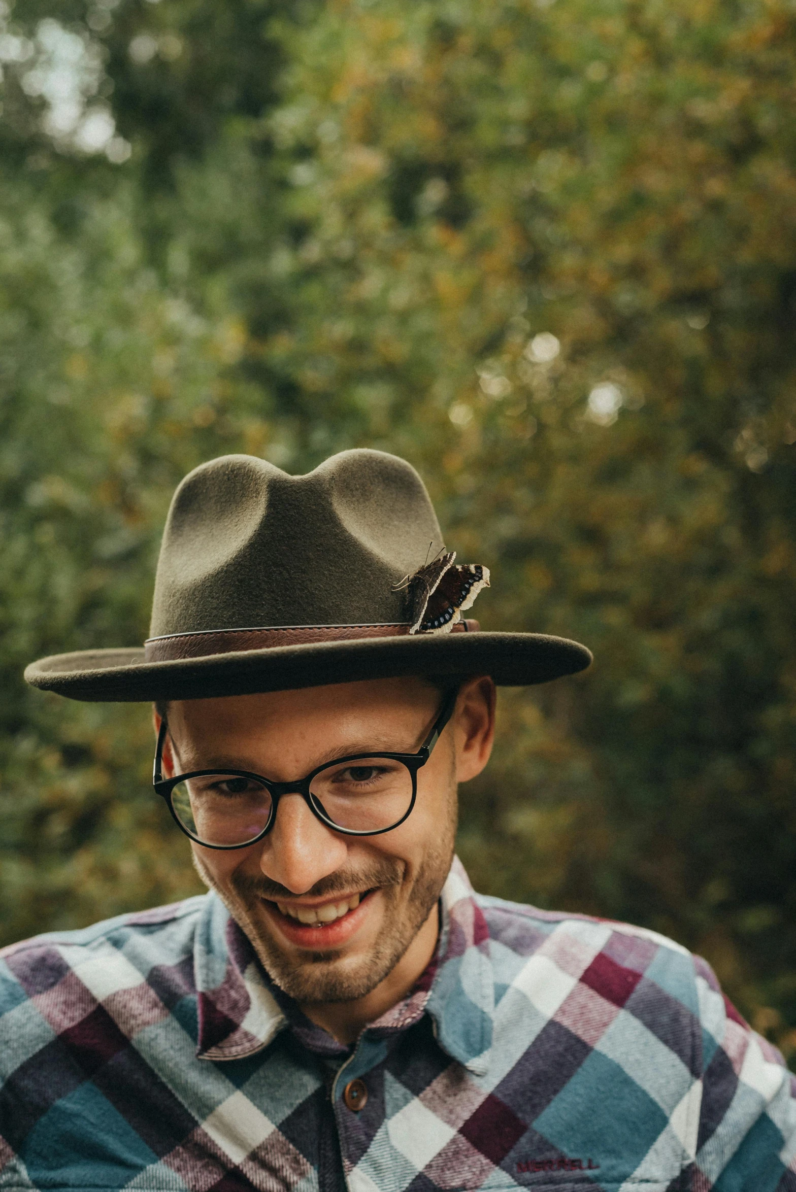 a man smiling and wearing a brown hat with a plaid shirt